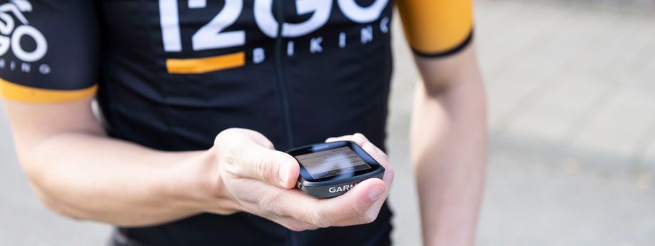 Garmin fietscomputer in hand van fietser met 12GO Biking fietsshirt