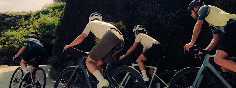 Groep racefietsers op de Scott Addict racefietsen die een bocht omhoog klimmen met een rotswand aan de binnenzijde