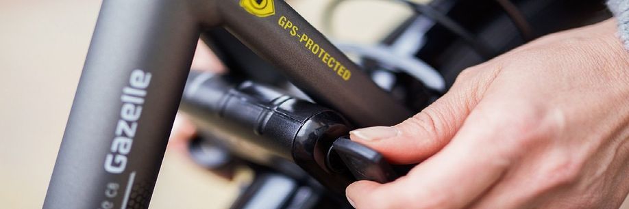 Fietser draait sleutel om van ringslot op een grijze Gazelle fiets die een GPS-Protected sticker heeft