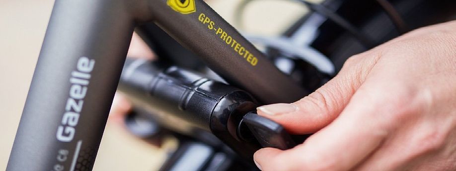 Fietser draait sleutel om van ringslot op een grijze Gazelle fiets die een GPS-Protected sticker heeft