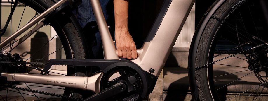 Man heeft hand op framebuis van champange kleur frame waarmee de e-bike met riemaandrijving opgetild kan worden