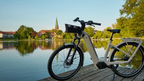 Beige Kalkhoff Image 5 op een houten steiger voor een meertje met gebouwen en een kerk achteraan