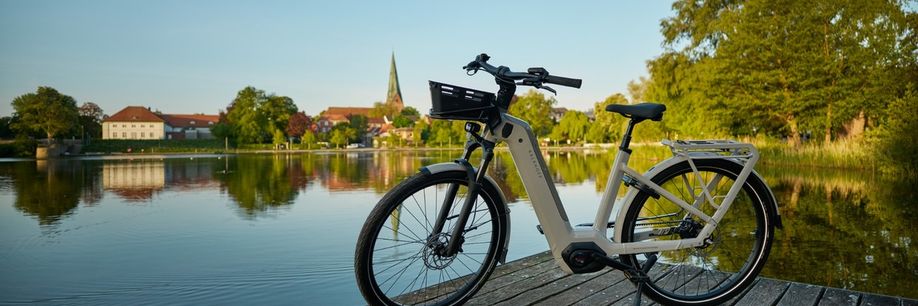 Beige Kalkhoff Image 5 op een houten steiger voor een meertje met gebouwen en een kerk achteraan