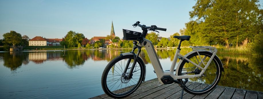 Beige Kalkhoff Image 5 op een houten steiger voor een meertje met gebouwen en een kerk achteraan