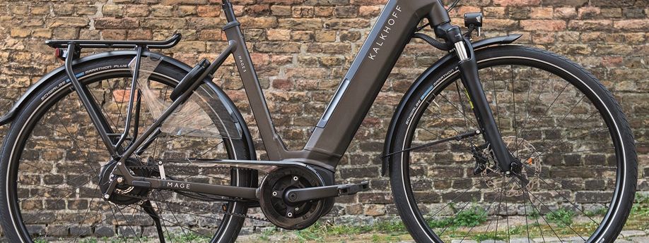 Bruine Kalkhoff Image e-bike op een kasseien ondergrond voor een oude stenen muur met een deel mos
