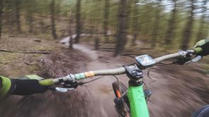 POV vanaf een mountainbiker op een groene MTB met oranje wielen die met snelheid over een trail in het bos afdaalt