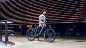 Man loopt met Riese & Müller speed pedelec in zijn hand hand een gebouw met houten buitenkant en ruiten erachter