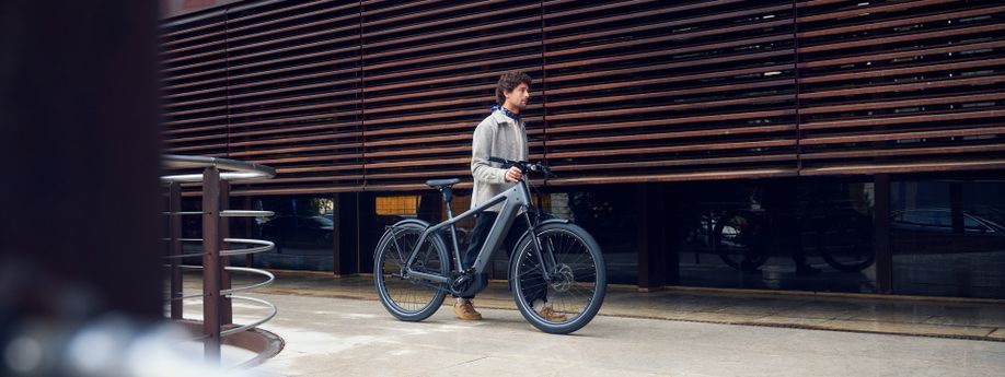 Man loopt met Riese & Müller speed pedelec in zijn hand hand een gebouw met houten buitenkant en ruiten erachter