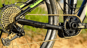 Mountainbike met SRAM Eagle XX1 groepset met gouden ketting en cassette met zand en gras op de achtergrond