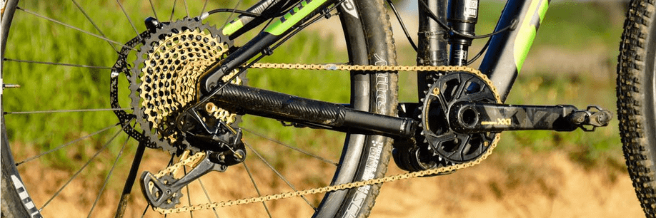 Mountainbike met SRAM Eagle XX1 groepset met gouden ketting en cassette met zand en gras op de achtergrond