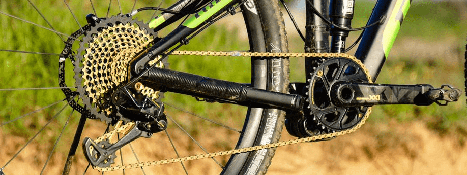 Mountainbike met SRAM Eagle XX1 groepset met gouden ketting en cassette met zand en gras op de achtergrond