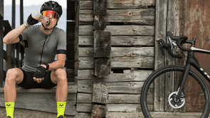 Man met Trek racefiets neemt pauze bij een houten hutje in de bergen terwijl hij wat sportvoeding dringt uit zijn bidon