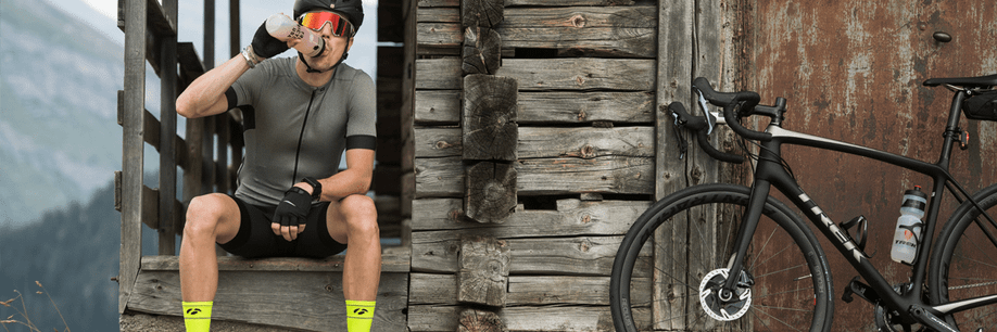 Man met Trek racefiets neemt pauze bij een houten hutje in de bergen terwijl hij wat sportvoeding dringt uit zijn bidon