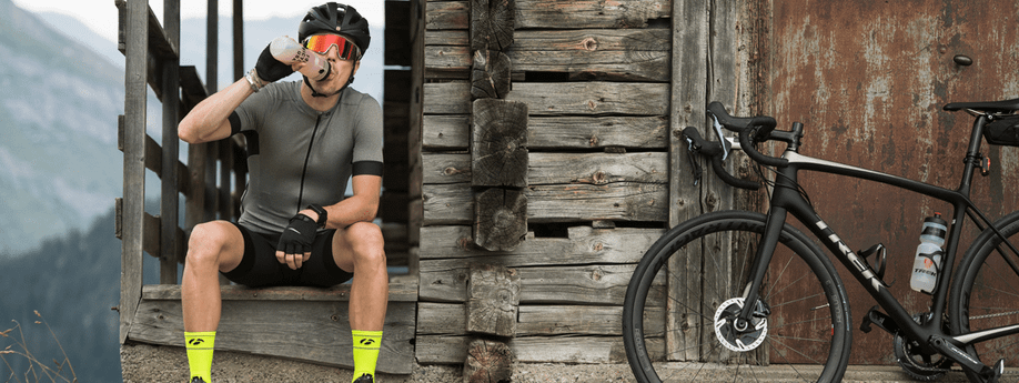 Man met Trek racefiets neemt pauze bij een houten hutje in de bergen terwijl hij wat sportvoeding dringt uit zijn bidon