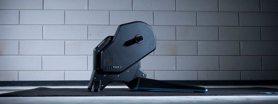 Tacx Flux 2 fietstrainer op een zwarte Tacx trainermat voor een betongetegelde muur