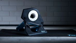 Tacx Neo 2T fietstrainer op een zwarte Tacx trainermat voor een betongetegelde muur