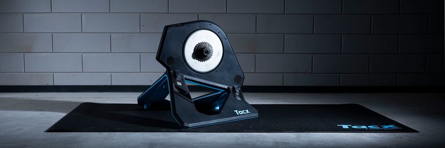 Tacx Neo 2T fietstrainer op een zwarte Tacx trainermat voor een betongetegelde muur