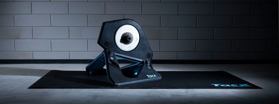 Tacx Neo 2T fietstrainer op een zwarte Tacx trainermat voor een betongetegelde muur