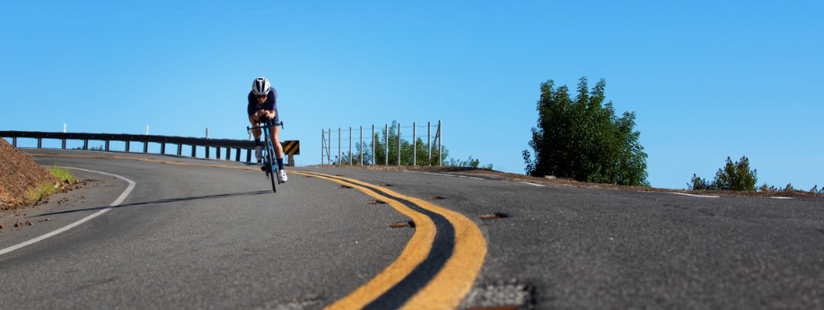 Triatleet op een Trek Speed Concept tijdritfiets die afdaalt over een asfaltweg met gele lijnen en een helderblauwe lucht