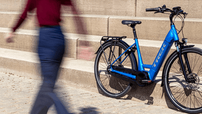 Vrouw loopt lang blauwe Trek e-bike die tegen een stenen trap aan staat