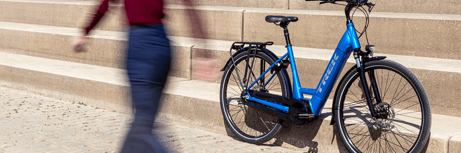 Vrouw loopt lang blauwe Trek e-bike die tegen een stenen trap aan staat