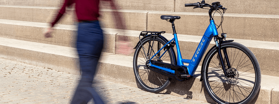 Vrouw loopt lang blauwe Trek e-bike die tegen een stenen trap aan staat