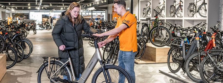 12GO Biking medewerker geeft uitleg over Batavus e-bike aan klant in de showroom van 12GO Biking met veel fietsen op achtergrond