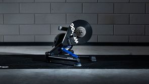 Wahoo Kickr Power V6 fietstrainer op een zwarte Wahoo trainermat met betongetegelde muur erachter