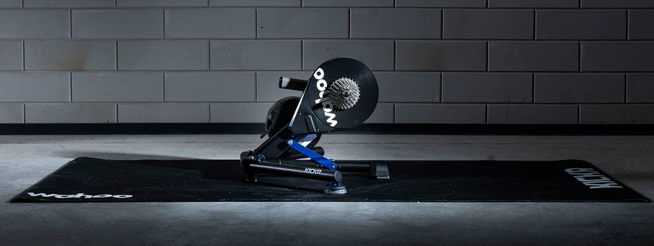 Wahoo Kickr Power V6 fietstrainer op een zwarte Wahoo trainermat met betongetegelde muur erachter