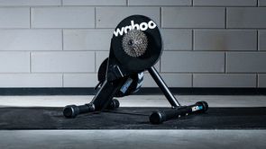 Wahoo Kickr Core fietstrainer op een zwarte Wahoo trainermat met betongetegelde muur als achtergrond