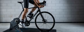 Fietser op Tacx Flux fietstrainer met Merida racefiets in 12GO Biking fietskleding voor betonnen muur