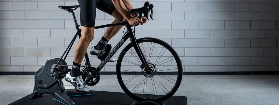 Fietser op Tacx Flux fietstrainer met Merida racefiets in 12GO Biking fietskleding voor betonnen muur