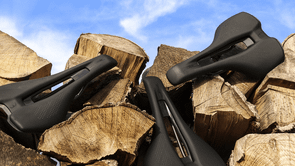 Verschillende zwarte fietszadels op stukken boomstammen voor een heldere blauwe lucht met kleine wolken