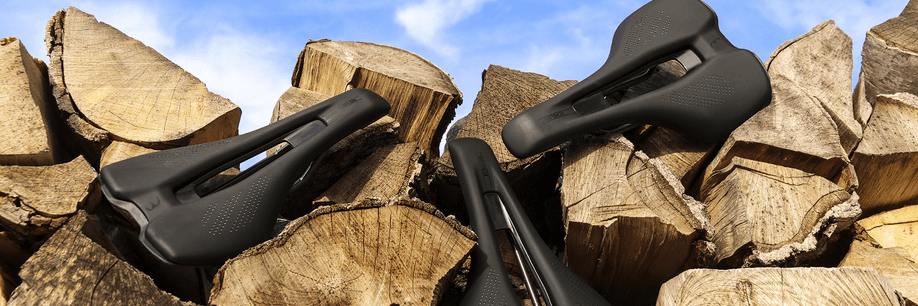 Verschillende zwarte fietszadels op stukken boomstammen voor een heldere blauwe lucht met kleine wolken