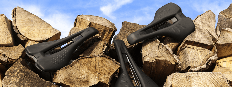 Verschillende zwarte fietszadels op stukken boomstammen voor een heldere blauwe lucht met kleine wolken