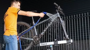 Grijze Trek mountainbike op Tacx standaard wordt afgespoten met tuinslag door persoon met 12GO Biking shirt