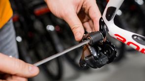 Persoon draait een bout van de achterderailleur los door midden van een een lange inbussleutel