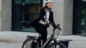 Vrouw met witte helm op elektrische Kalkhoff fiets met een voorlicht dat aanstaat in de stad met betegelde straat