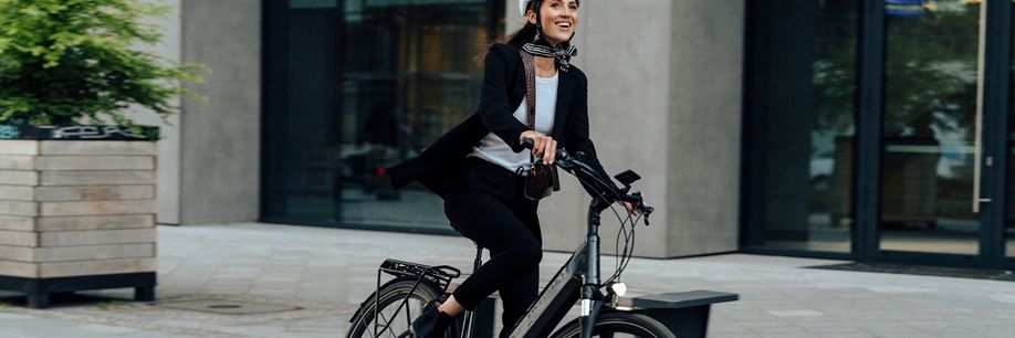 Vrouw met witte helm op elektrische Kalkhoff fiets met een voorlicht dat aanstaat in de stad met betegelde straat
