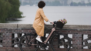Vrouw met roze Kalkhoff fiets heeft bloemen in haar mandje voorop en staat op een stenen brug over de rivier uit te kijken