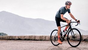 Fietser op Trek racefiets rijd over een weg met klein stenen muurtje hoog in de bergen naar boven met gekleurde schoenen