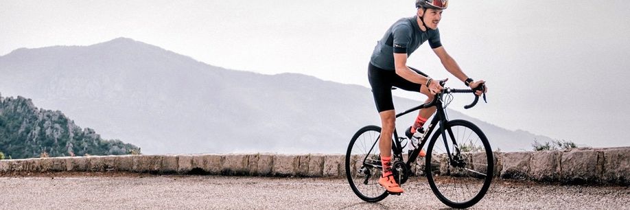 Fietser op Trek racefiets rijd over een weg met klein stenen muurtje hoog in de bergen naar boven met gekleurde schoenen