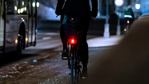 fietser met fel achterlicht naast een bus in op een donkere winteravond