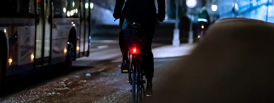 fietser met fel achterlicht naast een bus in op een donkere winteravond