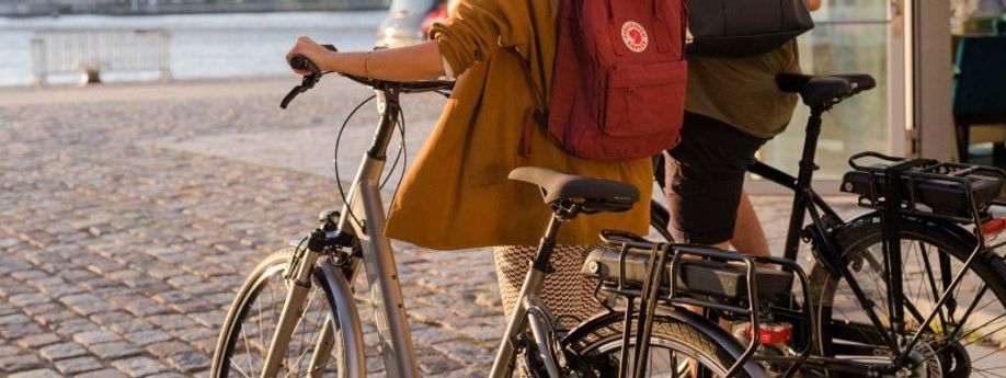 Mannelijke en vrouwelijke fietser lopen met e-bike met accu in bagagedrager over kasseien naar het water