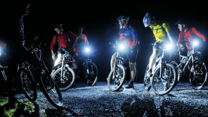 Groep mountainbikers die stil staat in het donker met felle verlichting op een gravelpad