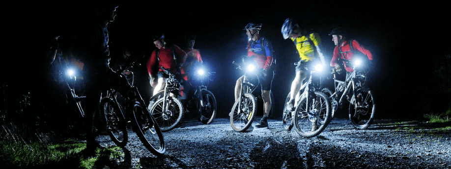 Groep mountainbikers die stil staat in het donker met felle verlichting op een gravelpad