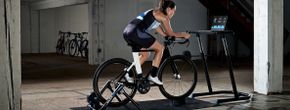Vrouwelijke fietser op zwarte fiets op Wahoo Kickr Snap met tabletscherm voor zich met een work-out, fietsen in de loods geparkeerd