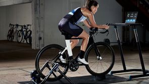 Vrouwelijke fietser op zwarte fiets op Wahoo Kickr Snap met tabletscherm voor zich met een work-out, fietsen in de loods geparkeerd