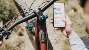 Fietser met rode mountainbike die voorzien is van een Bosch System Controller en Mini Remote terwijl hij de e-bike Flow app op zijn telefoon in de hand heeft